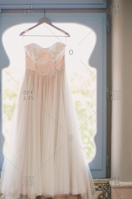 White Wedding Gown On A Wooden Hanger In Front Of A Window Stock