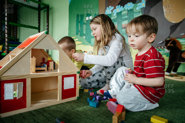 Children playing with a wooden doll house and peg people in a play center