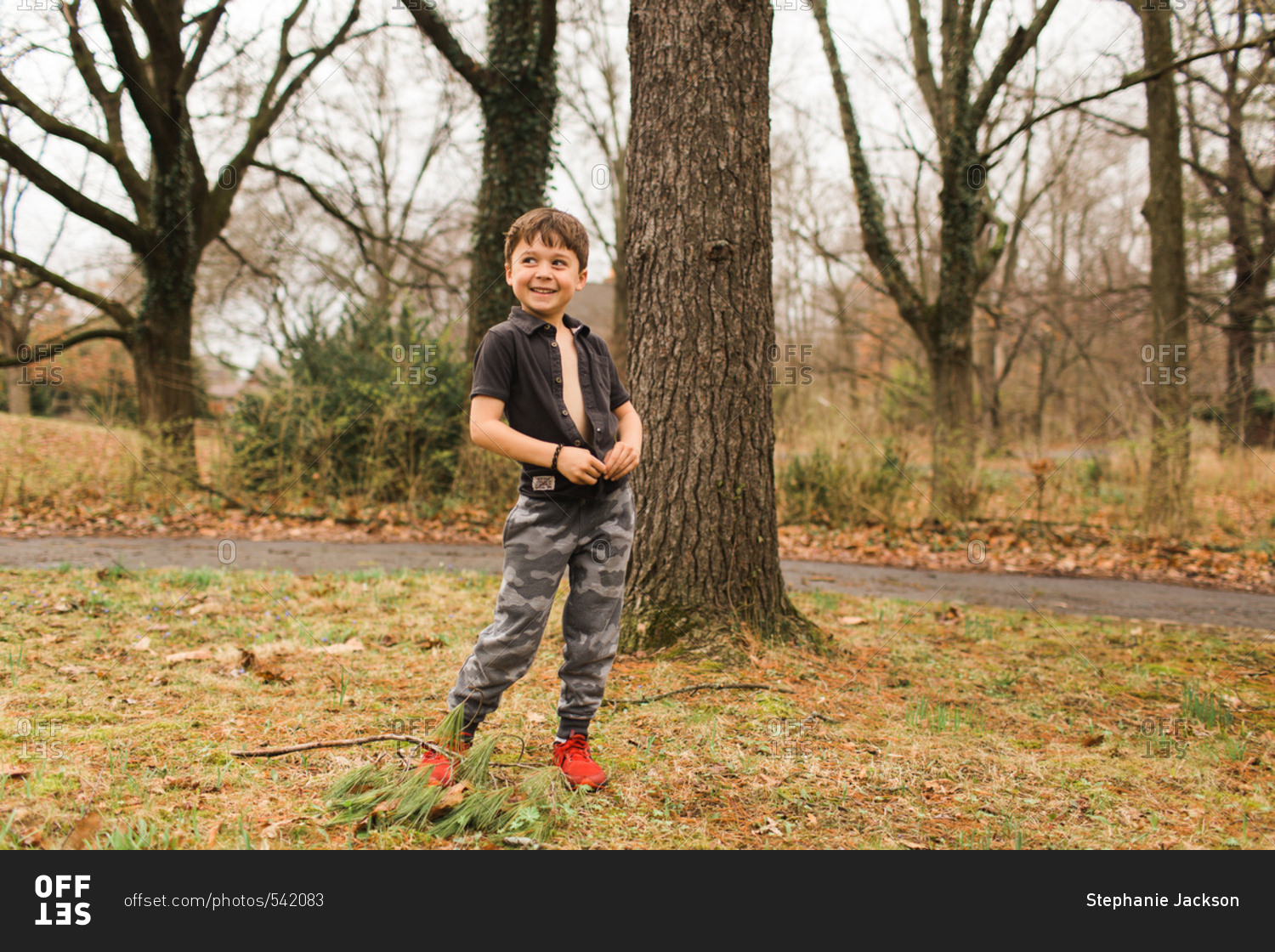 Little boy unbuttoning his shirt outside stock photo OFFSET