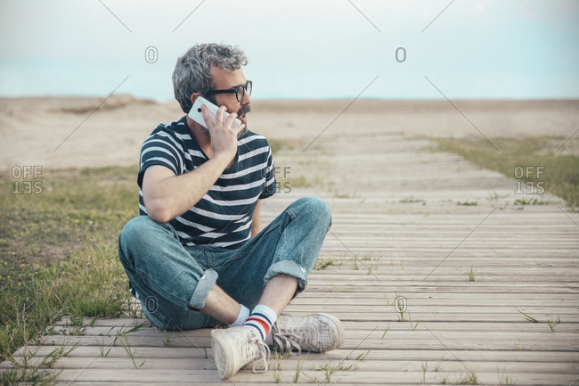 Man on the phone sitting on boardwalk looking at distance