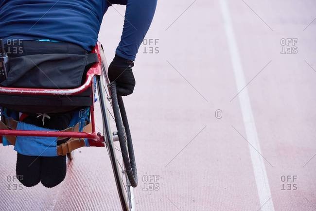 Preparing for Paralympics. Rear view of physically impaired athlete moving in racing wheelchair on track