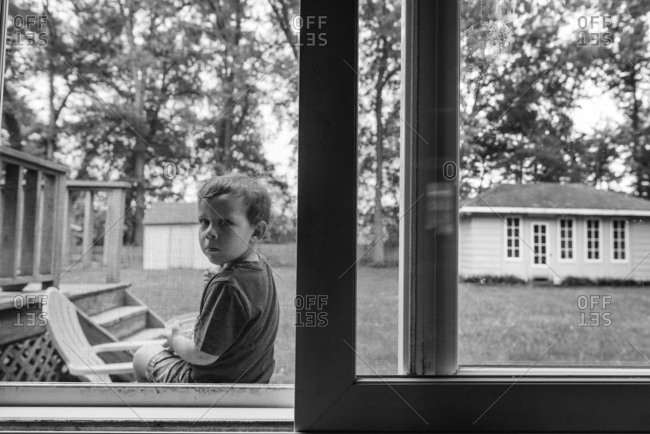 Boy sitting on a porch peering in through a screen door