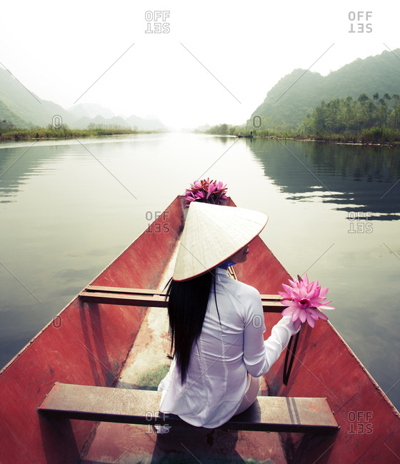 Vietnamese woman sitting on boat, holding lotus flower. Vietnam.
