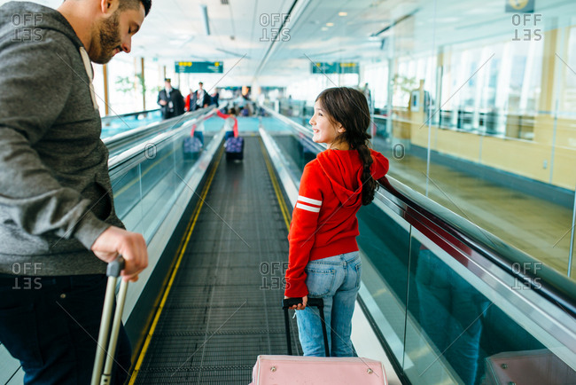 Girl on moving walkway in airport with father