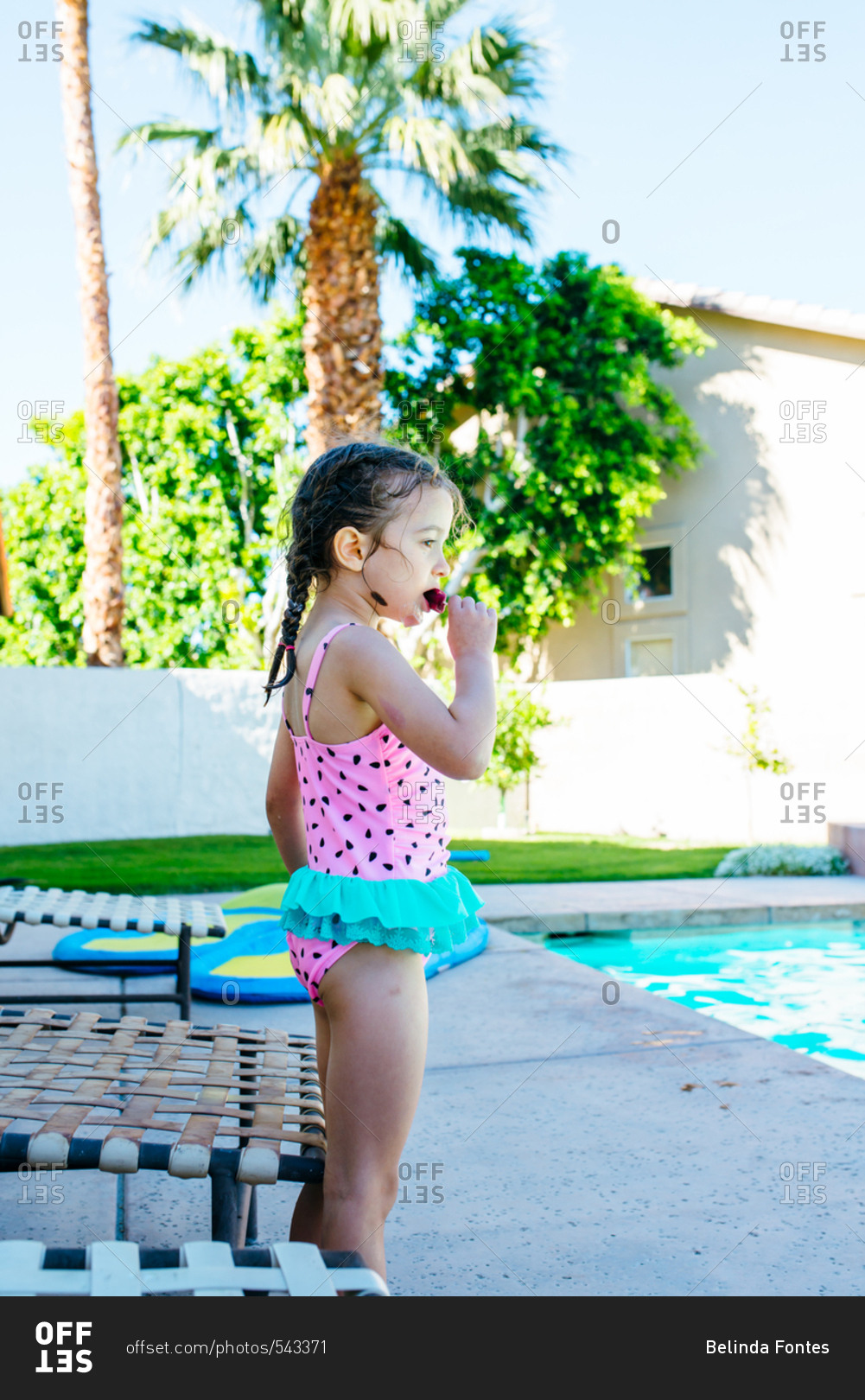 Young girl eating an ice pop by pool