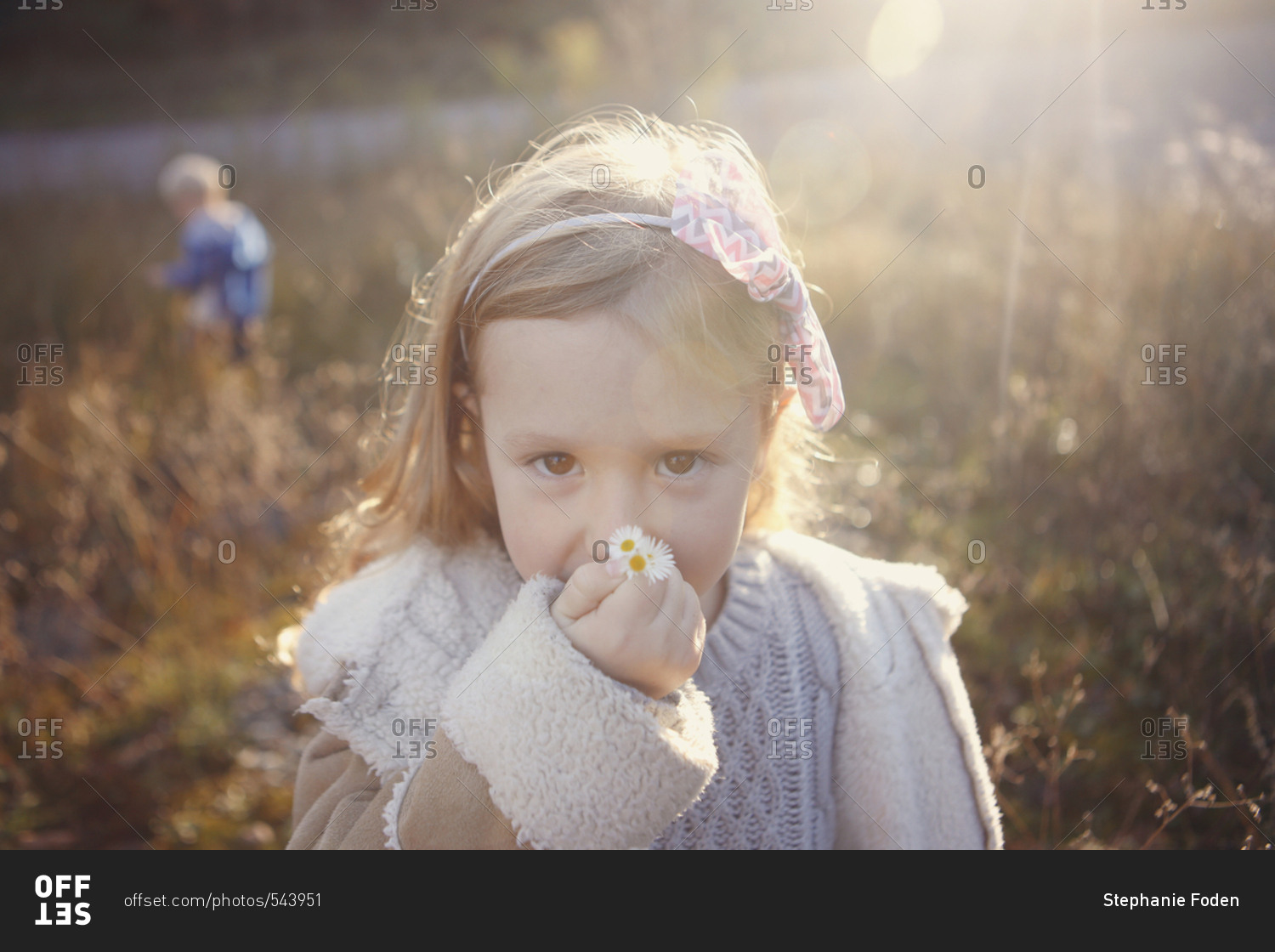 Young girl smelling small flowers in a sunny field