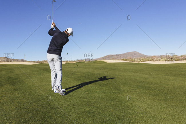 Rear view of golfer playing golf against on field against clear blue sky
