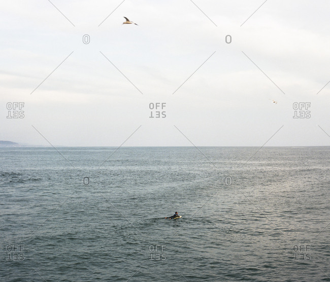 Distant view of man surfboarding in sea against sky