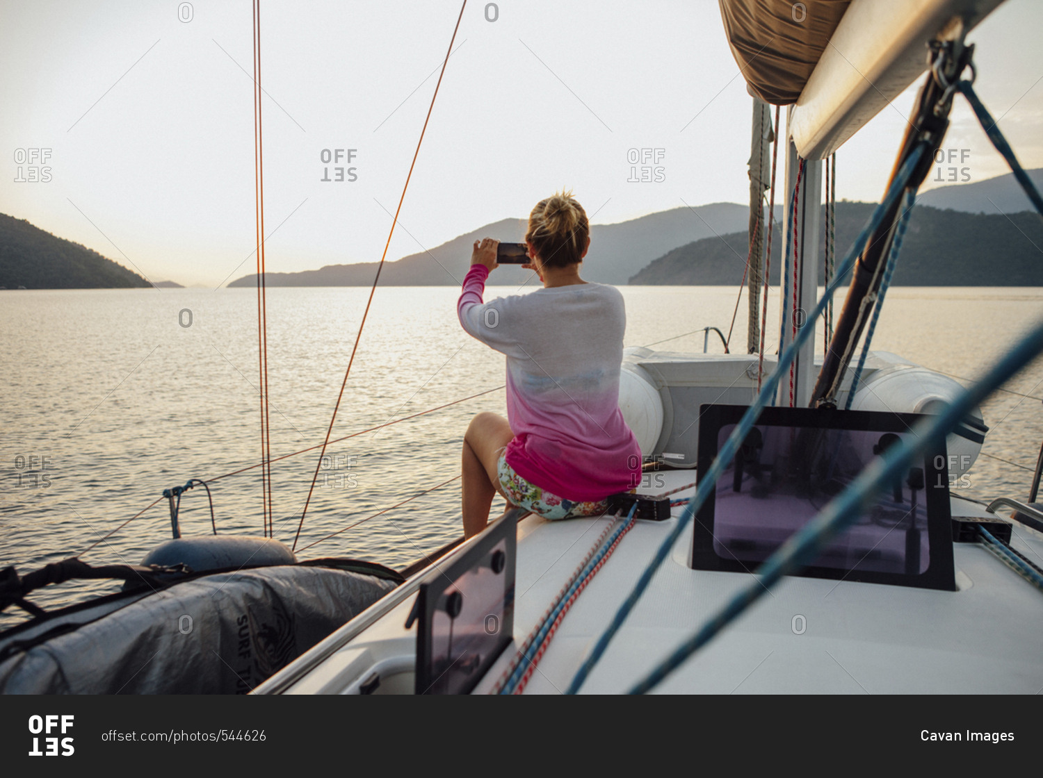 Rear view of woman photographing while traveling in sailboat on sea against clear sky
