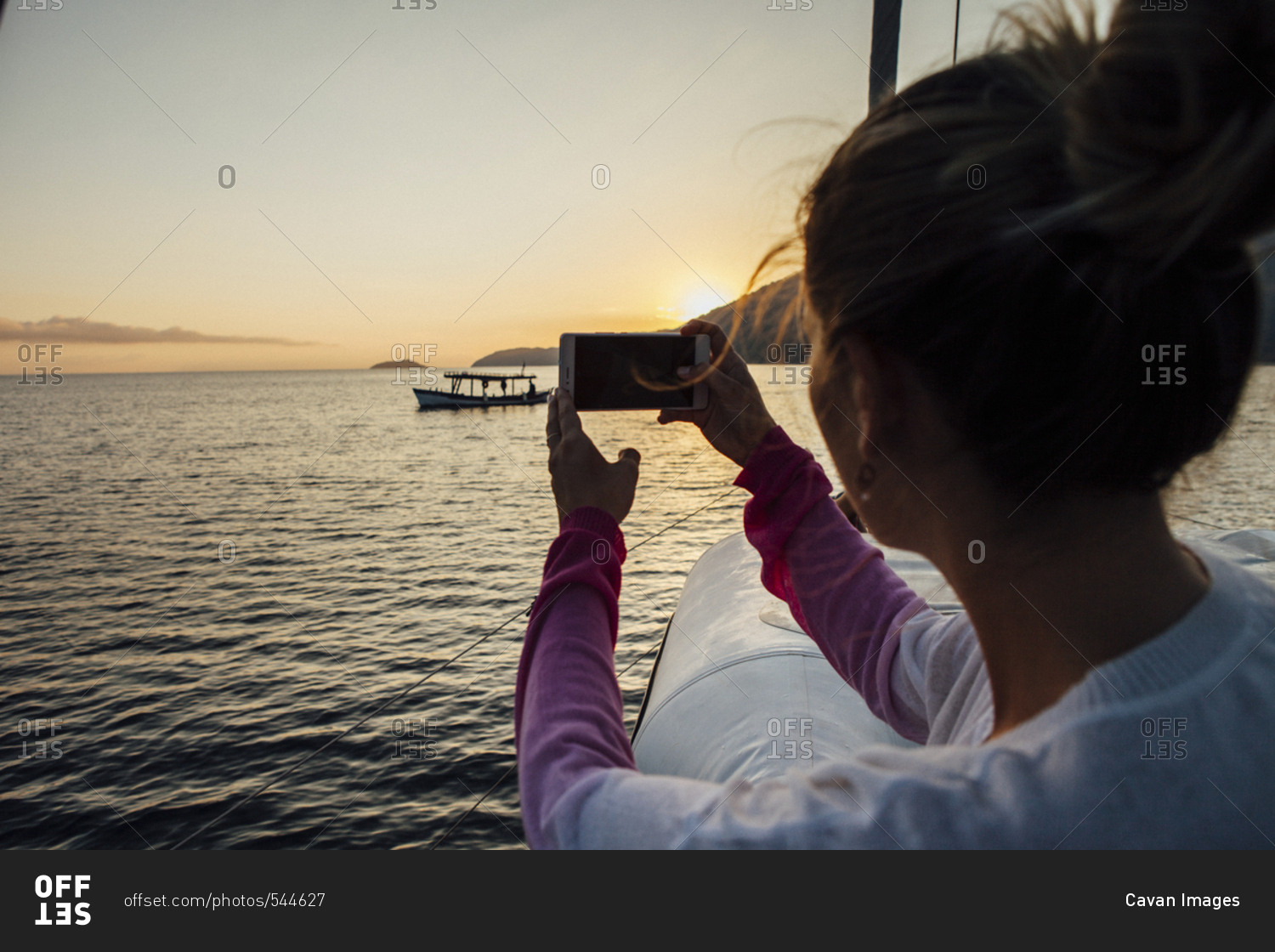 Woman photographing while traveling in sailboat on sea during sunset