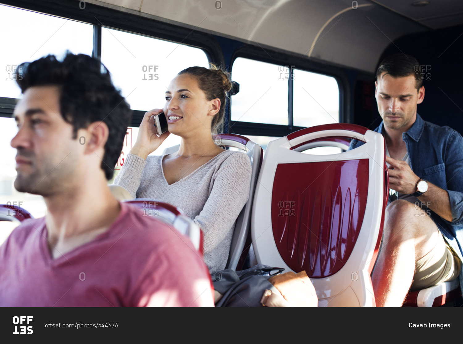 Woman talking on mobile phone while traveling with other passengers in tour bus