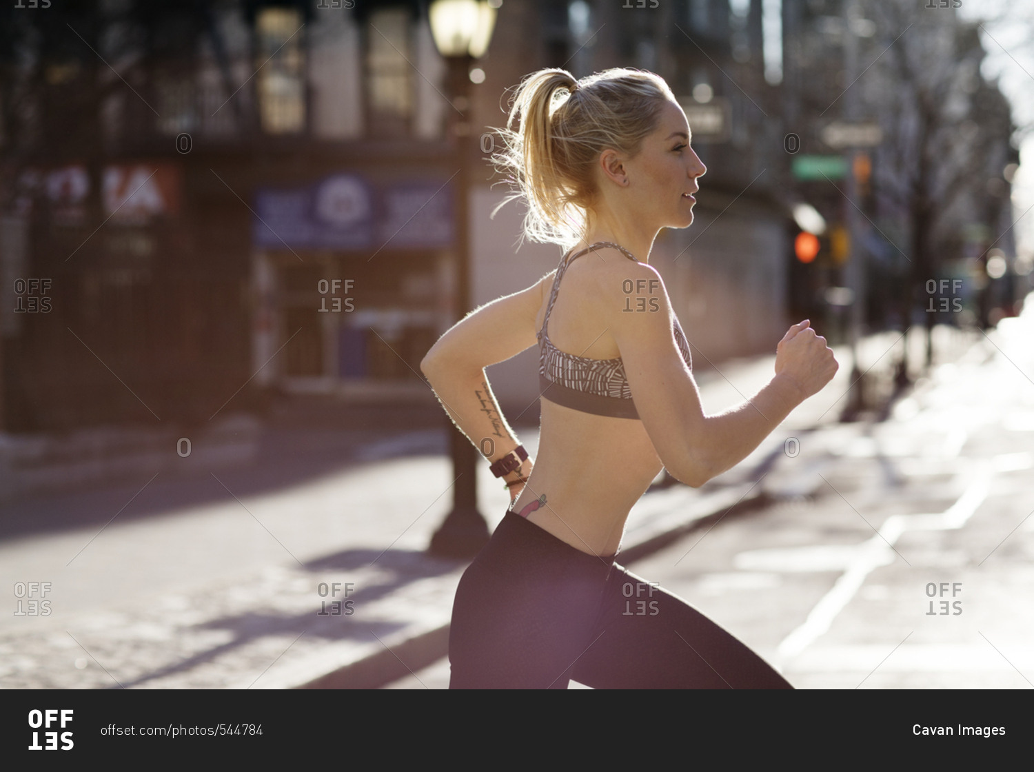 Side view of female athlete running on city street during sunny day