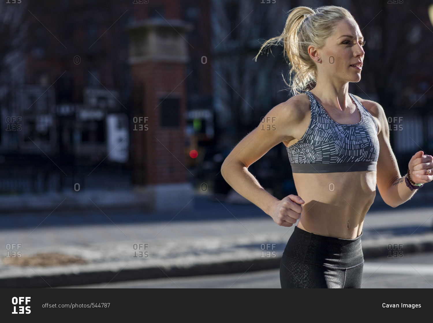 Female athlete running on street during sunny day stock photo - OFFSET