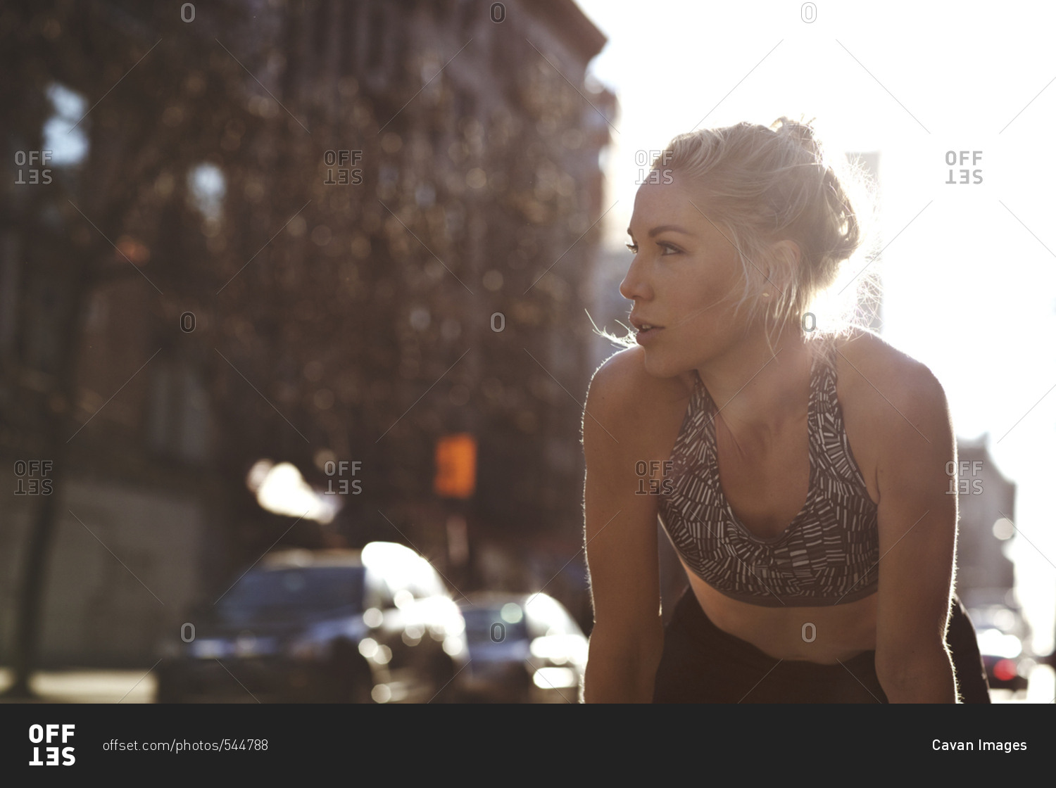 Tired athlete looking away while relaxing on street during sunny day