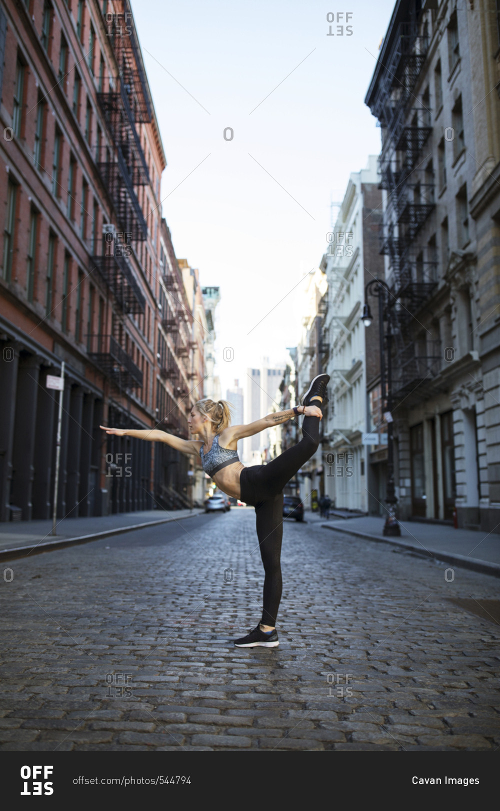 Female athlete exercising on street against sky in city