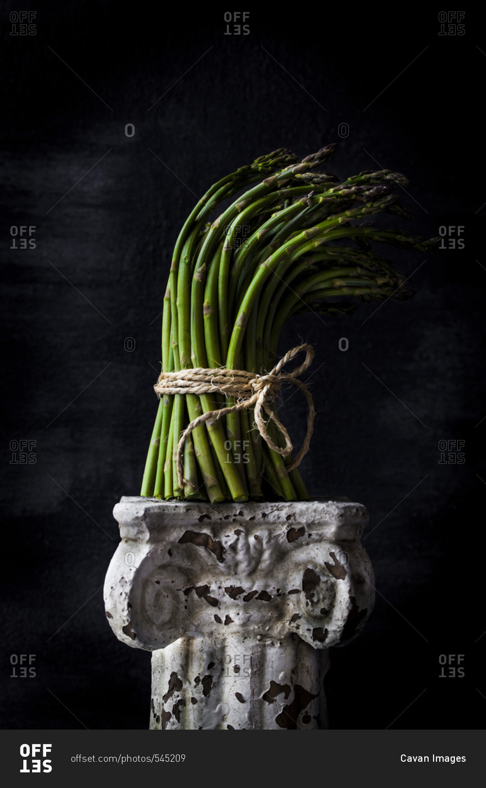Bunch of asparagus on old pedestal against black background