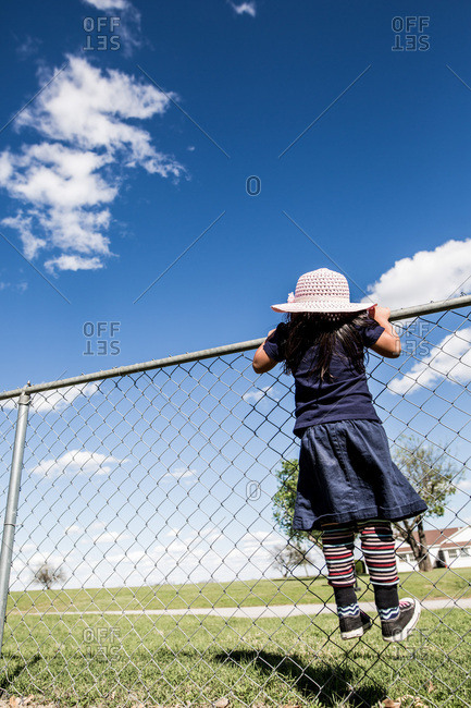 Girl wearing a pink hat peering over chain link fence