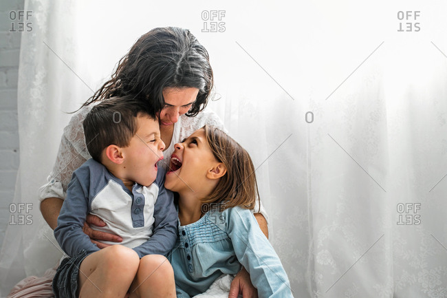 Mom cuddles her children while they make silly faces