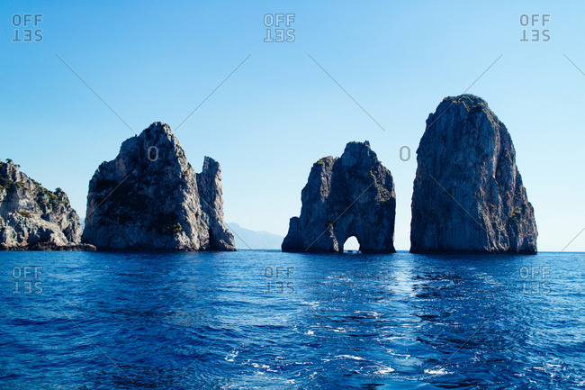 Distant boat steering through a  stone formation off the coast of Capri, Italy