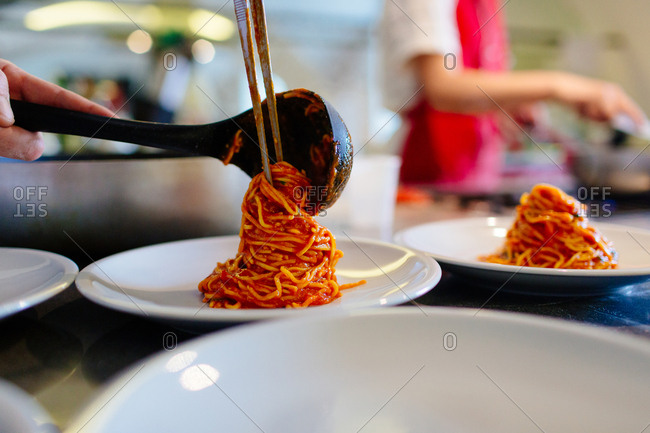 Person plating pasta noodles and tomato sauce on a plate