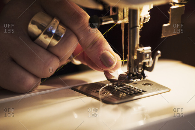 A woman's hand holding thread and threading a sewing machine needle