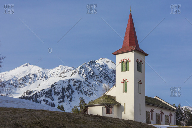The white alpine church framed by snowy peaks, Maloja, Bregaglia Valley, Canton of Graubunden, Engadine, Switzerland, Europe