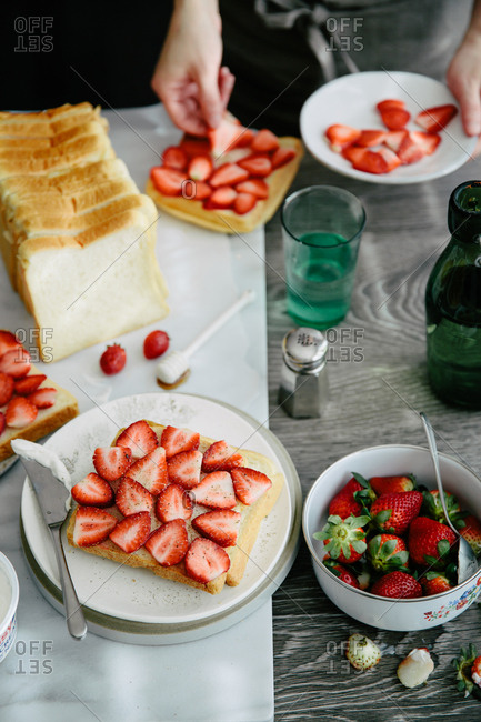 Person placing sliced strawberries on a piece of bread