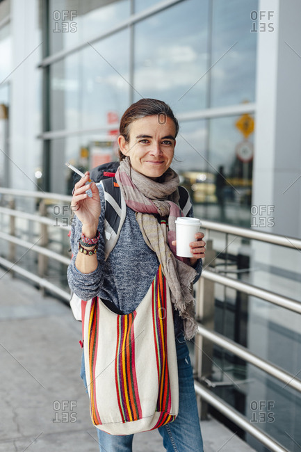 Portrait of a traveller woman smoking and having a cup of coffee outside the airport