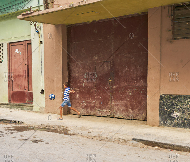 Havana, Cuba - March 3, 2017: Boy playing with soccer ball on sidewalk in Havana, Cuba