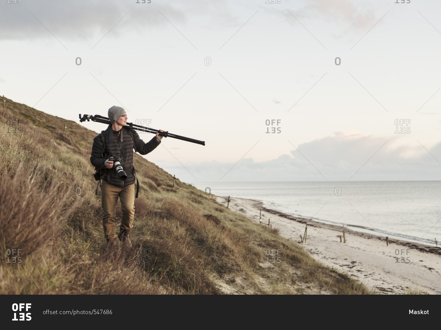 Photographer looking away while carrying tripod on hill by sea