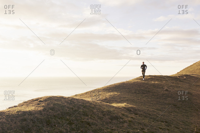 Mid distance of man jogging on hill by sea during sunny day
