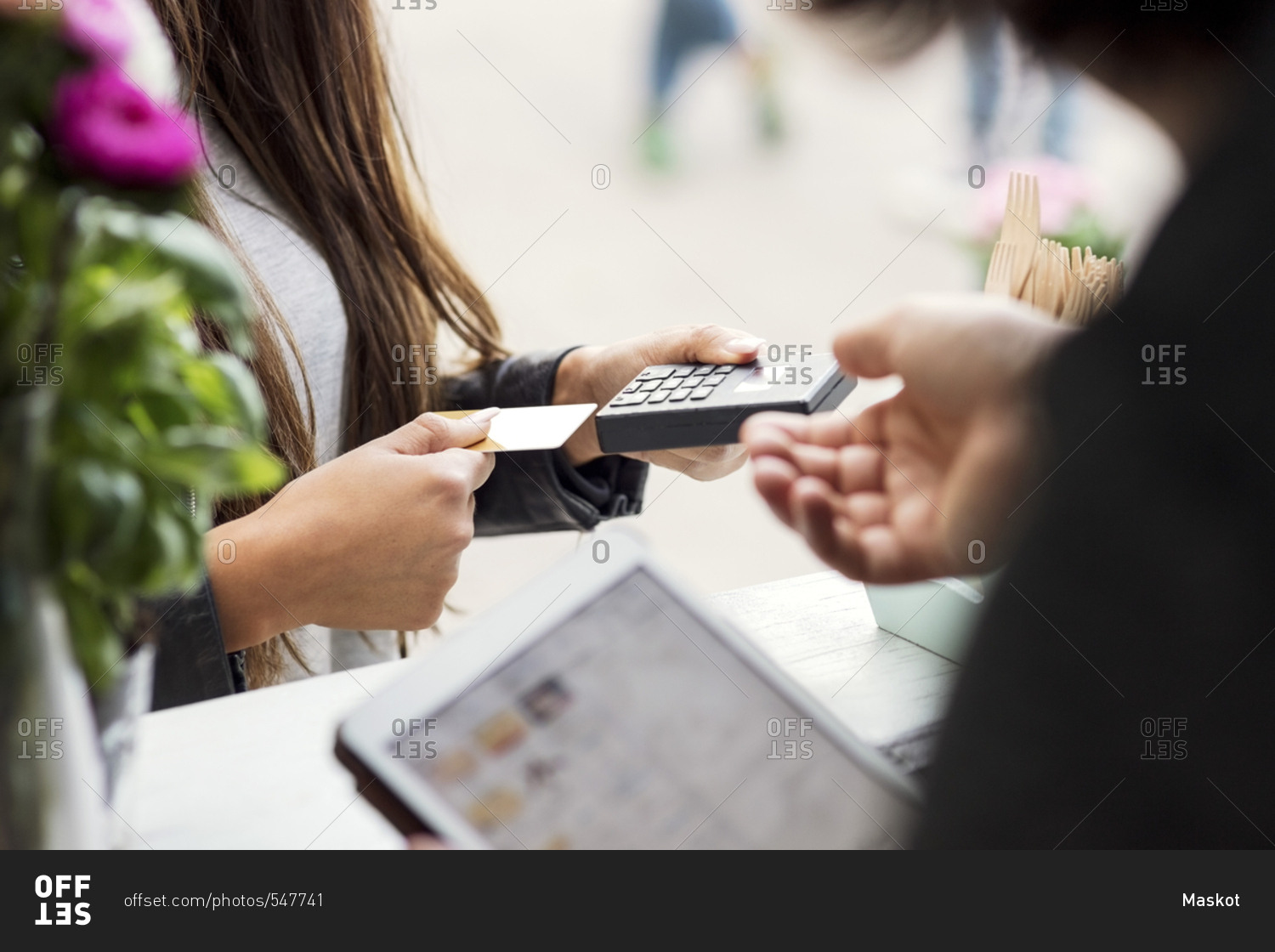 Midsection of female customer paying through card reader while owner holding digital tablet in food truck