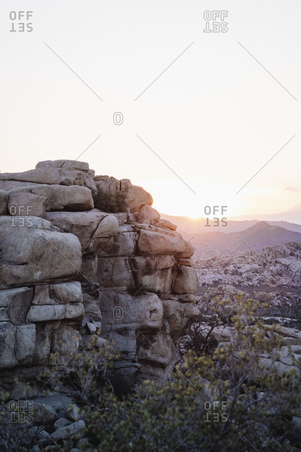 Sun setting behind rock formations and mountains in the desert