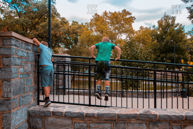 Twin Caucasian Brothers Stand and Climb Atop A Metal Handrail To Get Over A Rock Wall