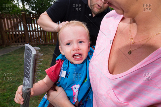 Toddler Boy Sits On Moms Lap In Backyard While He Gets His First