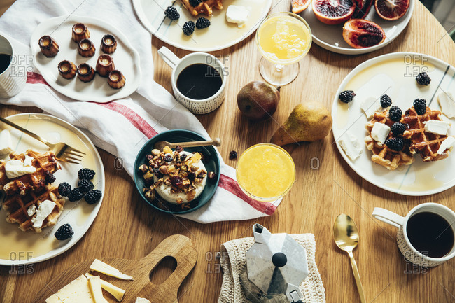 Decadent breakfast of waffles, pastries, fruit and cheese arranged on a wooden table