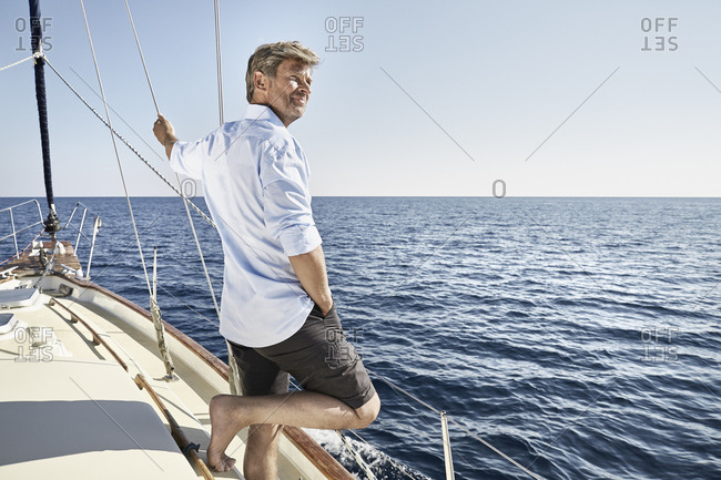Smiling mature man standing on his sailing boat looking at distance