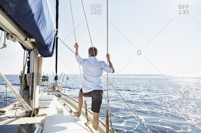 Back view of mature man standing on his sailing boat looking at distance