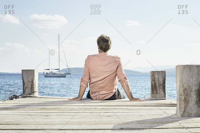 Back view of man sitting on jetty looking at distance