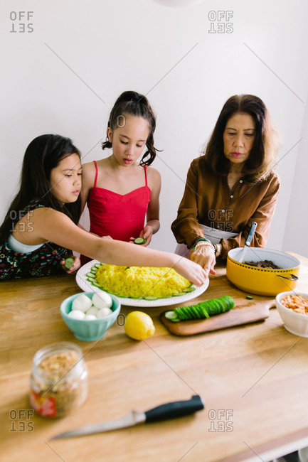 Two young girls help their grandmother prepare a traditional Indonesian meal