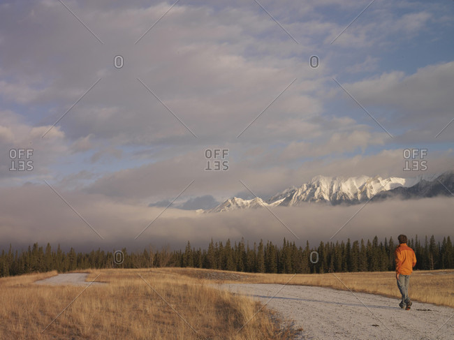 Man walks down windy road with fog and mountains in distance