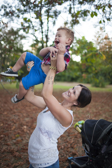 Mother Lifts Her Baby Into The Air Playfully At The Park
