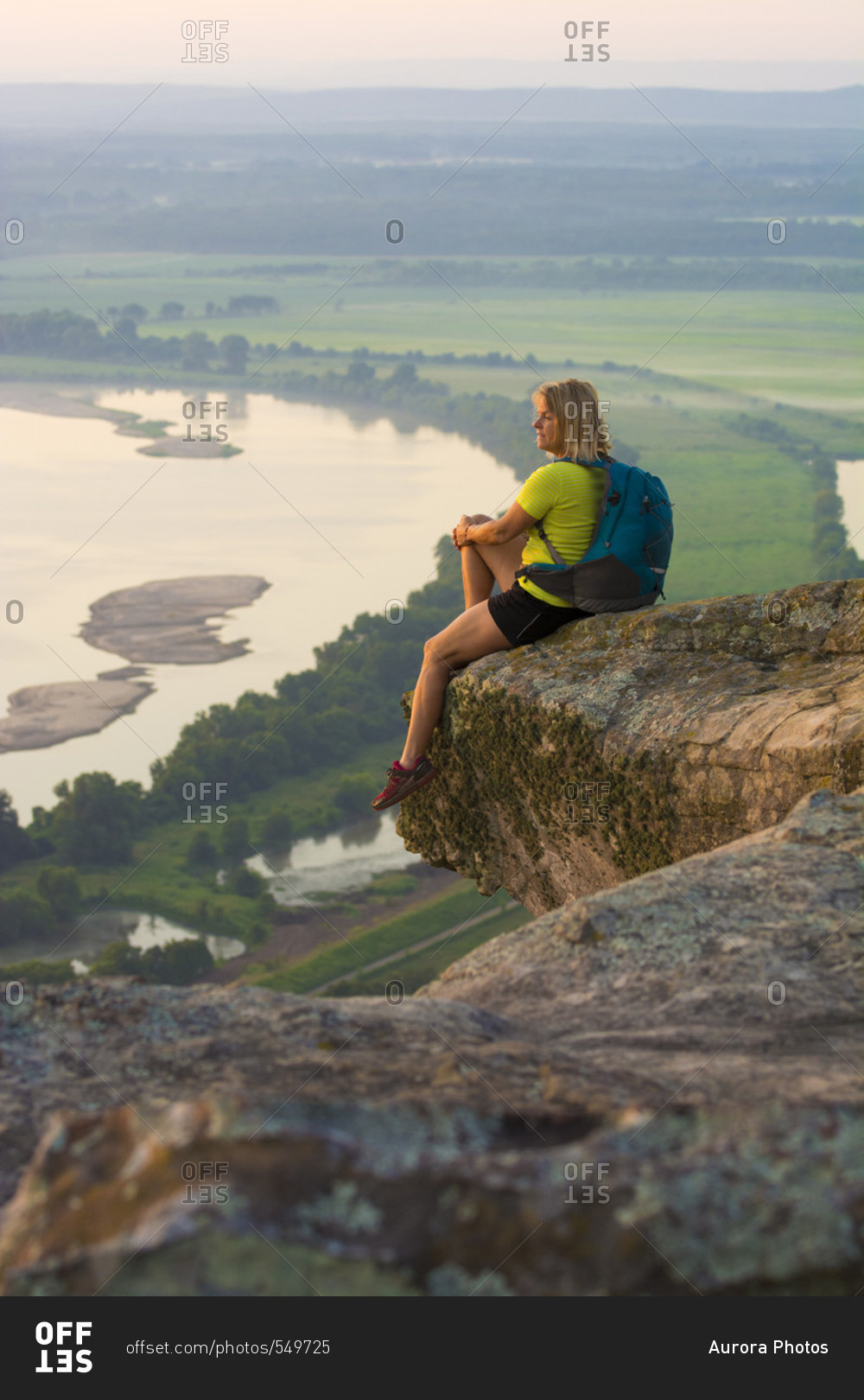 Woman sitting on sandstone overhang watching sunrise from summit of Petit Jean Mountain Above Arkansas River Valley?