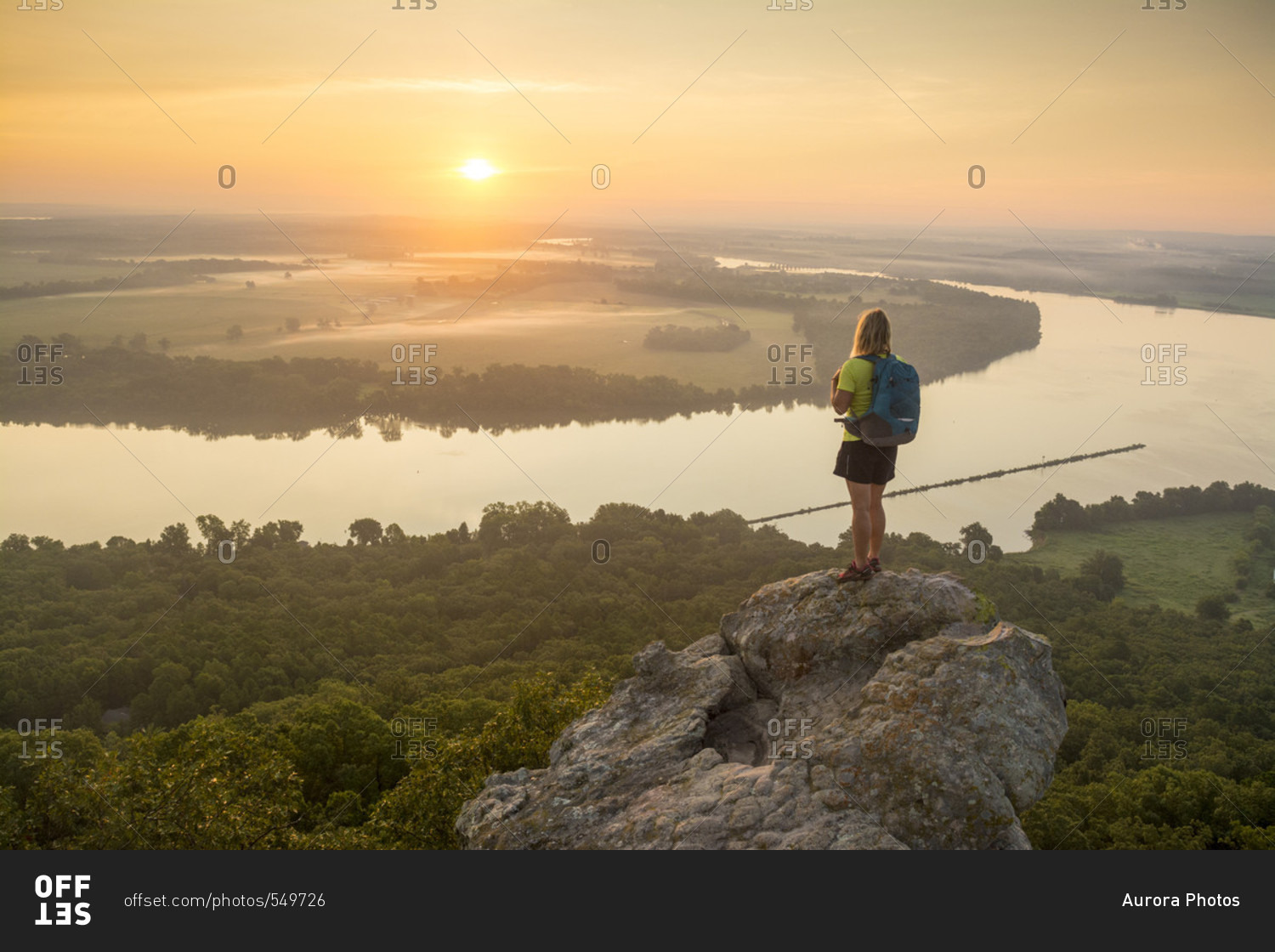Woman standing on sandstone overhang watching sunrise from summit of Petit Jean Mountain Above Arkansas River Valley?