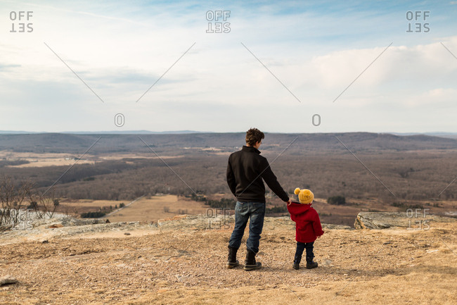 Father holding son's coat while walking on top of mountain