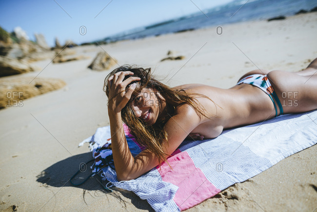 Woman lying on the beach without the bikini top looking at camera