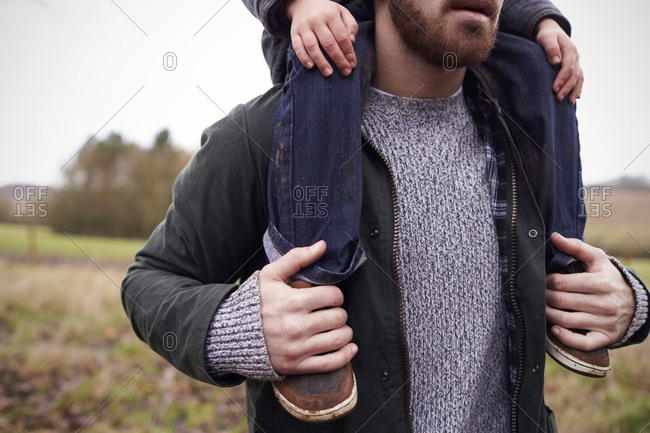 Close Up Of Father Gives Son Ride On Shoulders During Walk