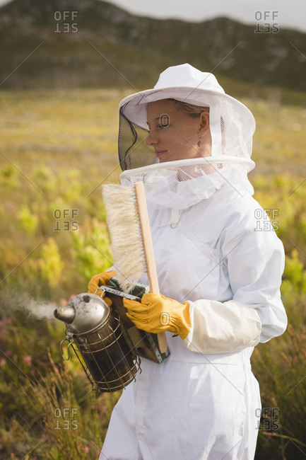 Female beekeeper holding bee smoker and brush on farm