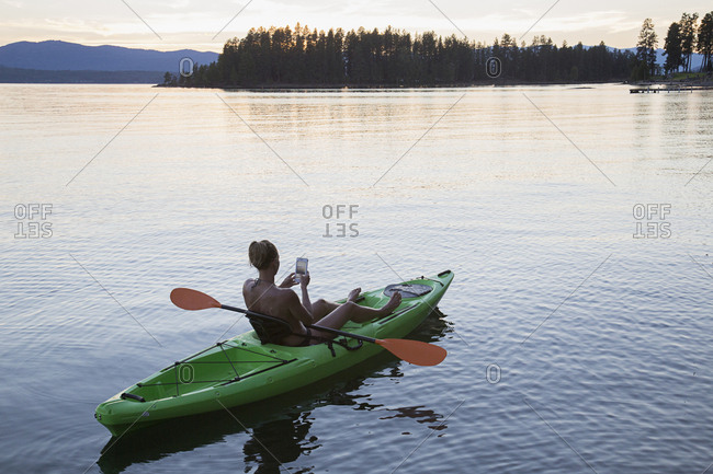 Caucasian woman in kayak on river texting on cell phone