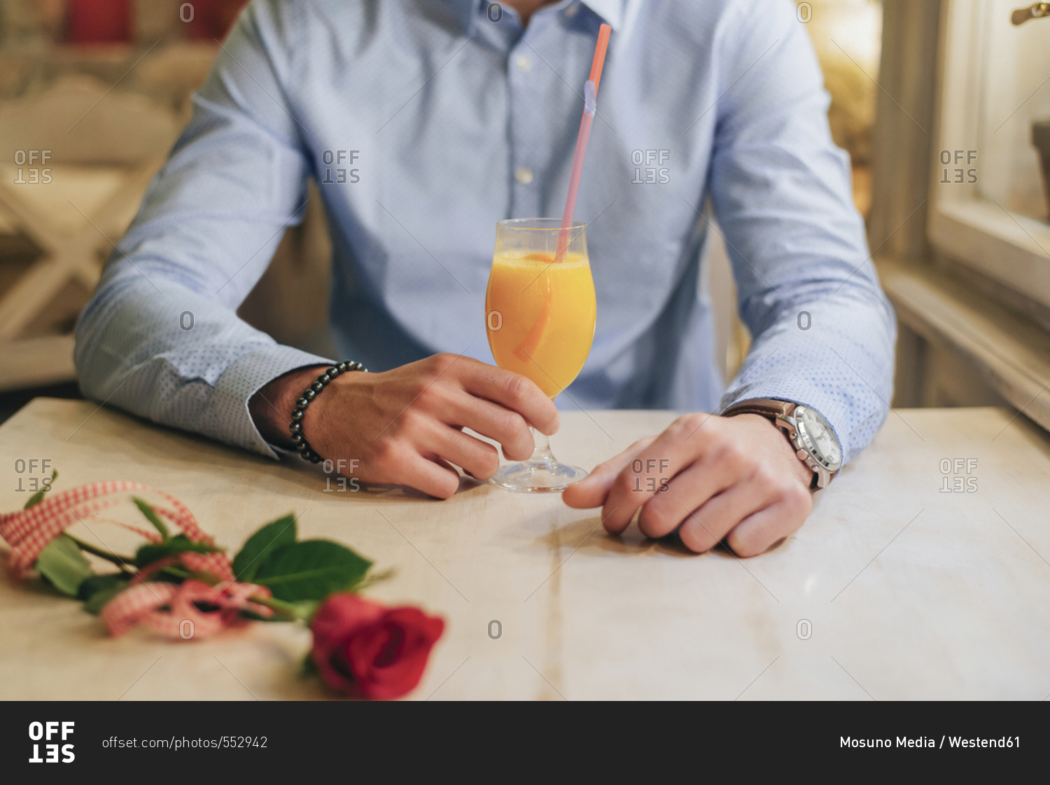 Waiting man with drink and red rose sitting at table- partial view